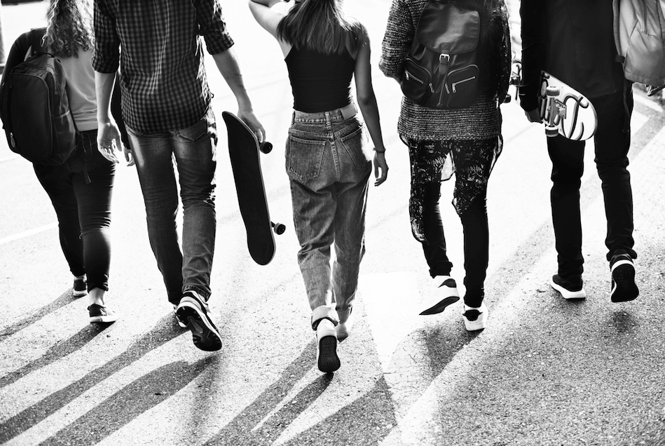 Black and white photo of group of teenagers walking with skateboards. 