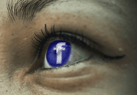 An eye reflecting the Facebook logo.